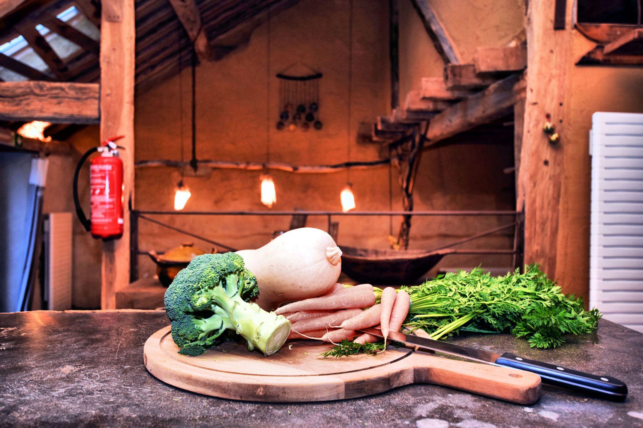 A wooden cutting board with vegetables and a knife on a kitchen counter.