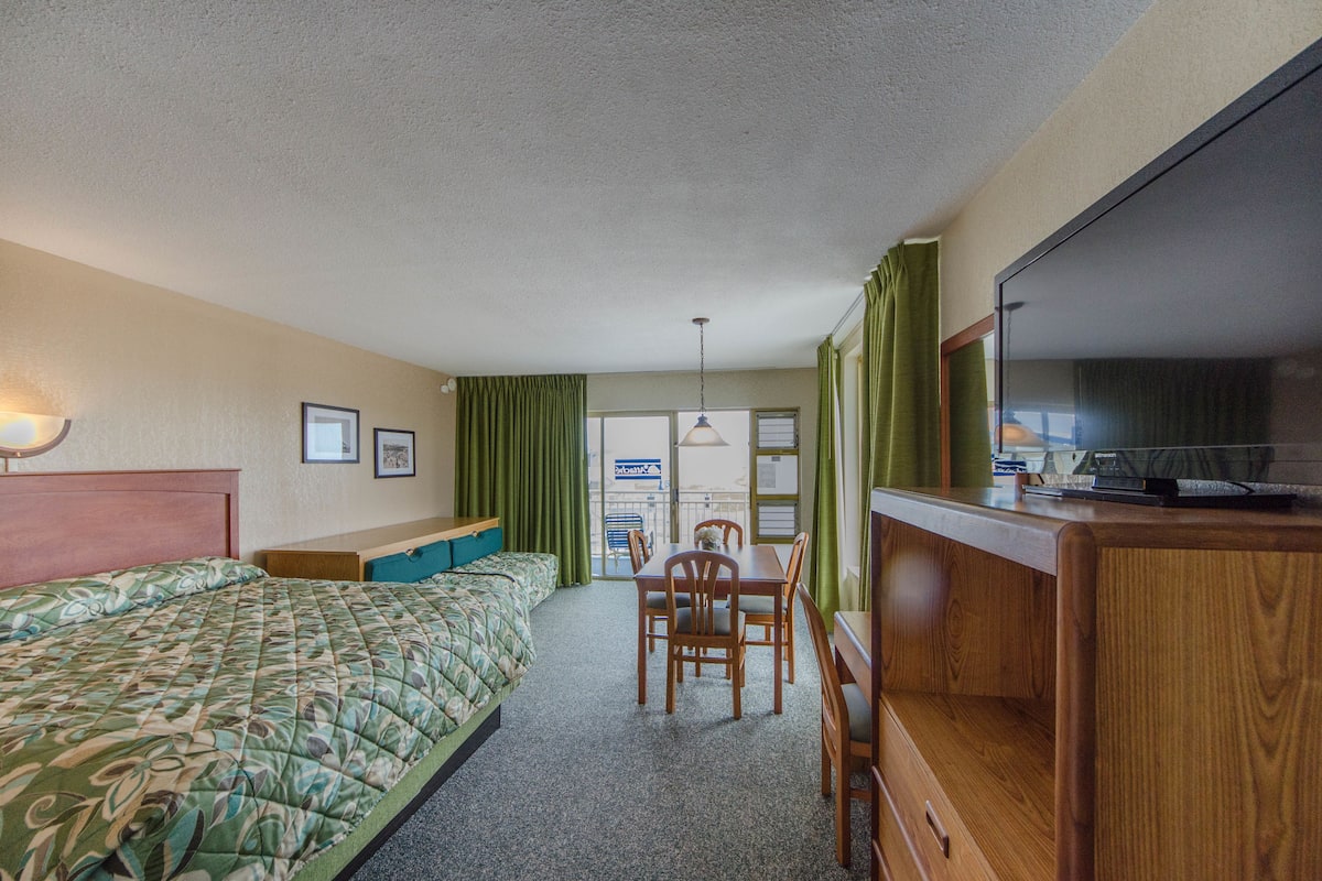Quarto de hotel com uma cama, uma escrivaninha e uma televisão.