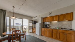 A kitchen with wooden cabinets, a refrigerator, a microwave, and a dining area with chairs and a table. - Attache Motel (Wildwood Crest)
