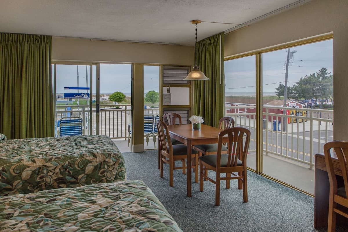 Quarto de hotel com duas camas, uma mesa de jantar com cadeiras, uma janela com vista para a praia e uma varanda com vista para a praia e um posto de salva-vidas.