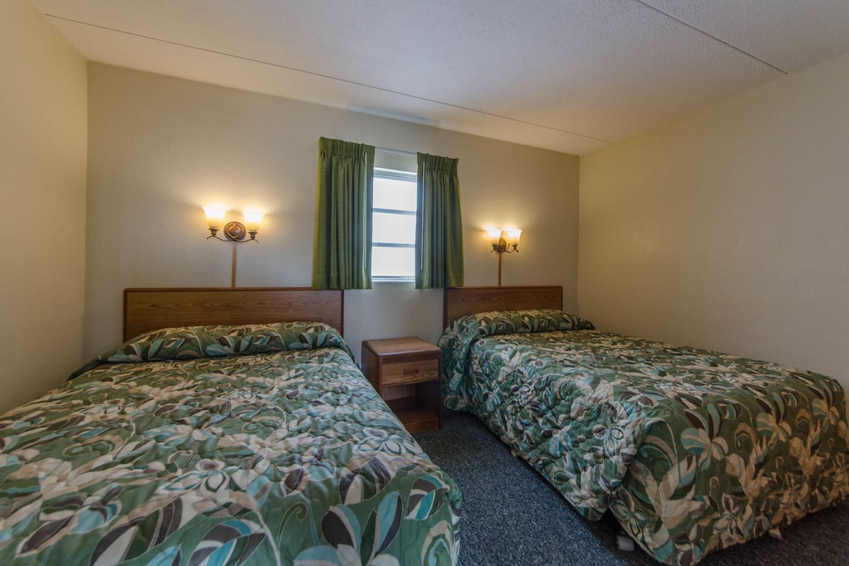 Quarto de hotel com duas camas, uma janela com cortinas e luminárias fixadas na parede.