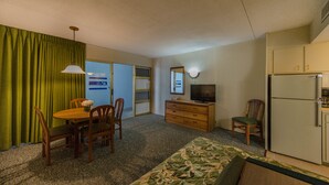 A compact hotel room with a dining table, chairs, a sofa, a television, a refrigerator, and a small kitchenette. - Attache Motel (Wildwood Crest)