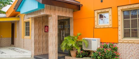 A building with a tiled entrance, a blue awning, and a potted plant with pink flowers.