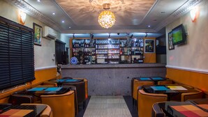 A bar area with a counter, shelves of bottles, and a television screen. There are tables and chairs arranged for seating. - Benestar Suites (Lagos)