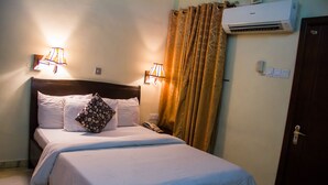 A hotel room with a bed, two bedside lamps, a curtain, an air conditioning unit, and a door. - Benestar Suites (Lagos)
