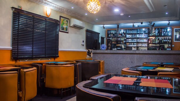 A bar area with tables and chairs, a bar counter with bottles, and a decorative light fixture. - Benestar Suites (Lagos)