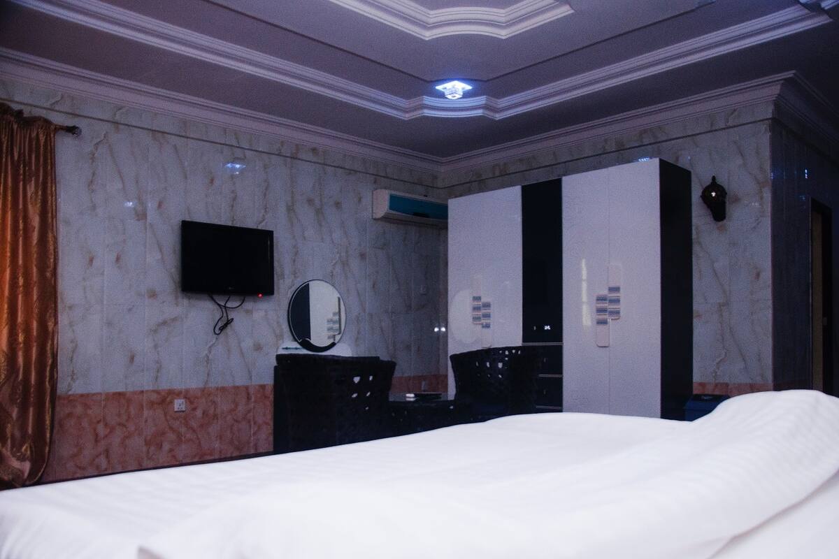 Habitación de hotel con cama, televisor de pantalla plana en la pared, espejo, cómoda y armario.