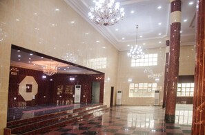 Um hall espaçoso com um lustre imponente, colunas de mármore e um chão quadriculado.