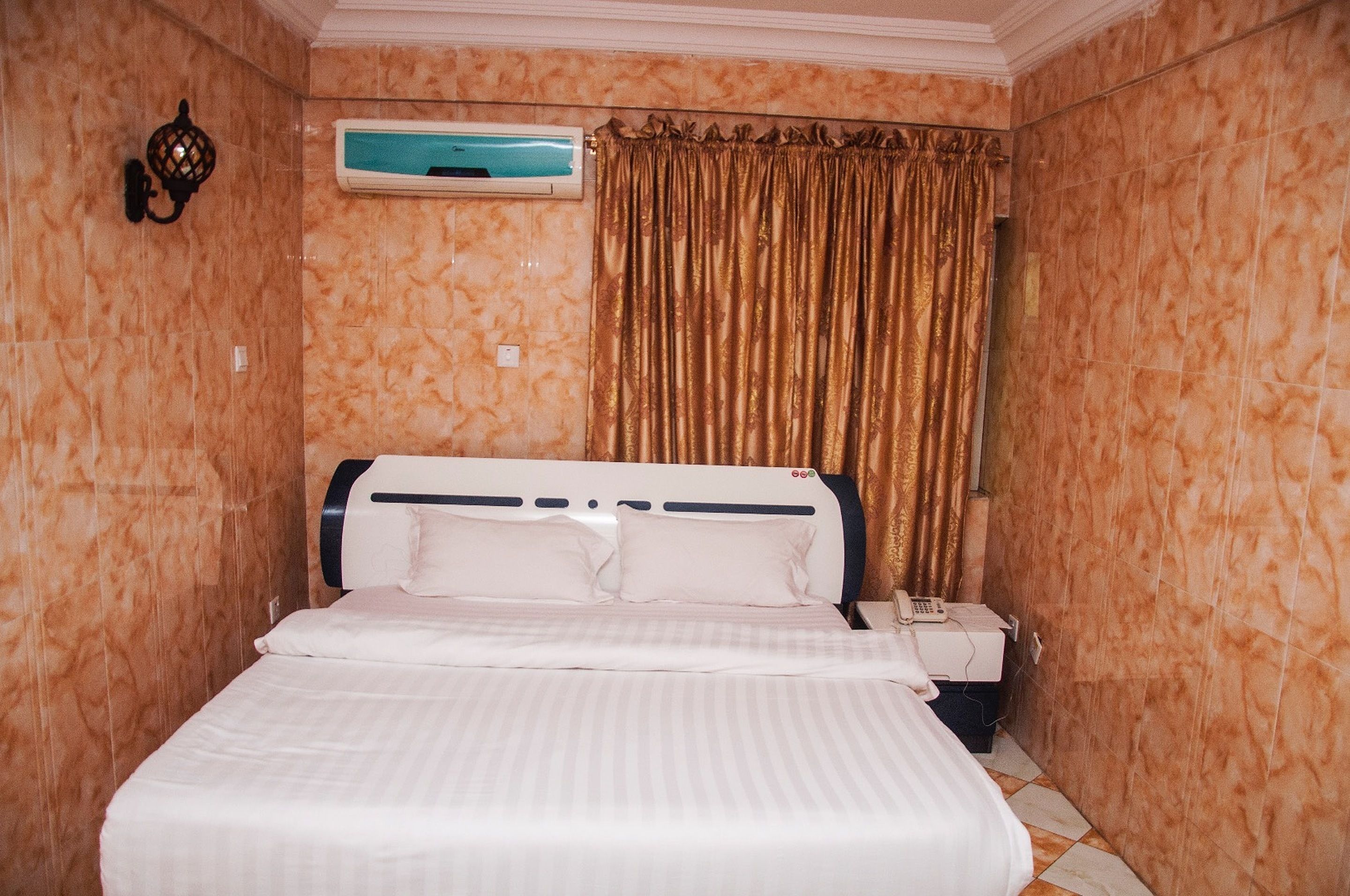 Une chambre d’hôtel équipée d’un lit, d’un appareil de climatisation, d’un téléphone et d’un rideau.