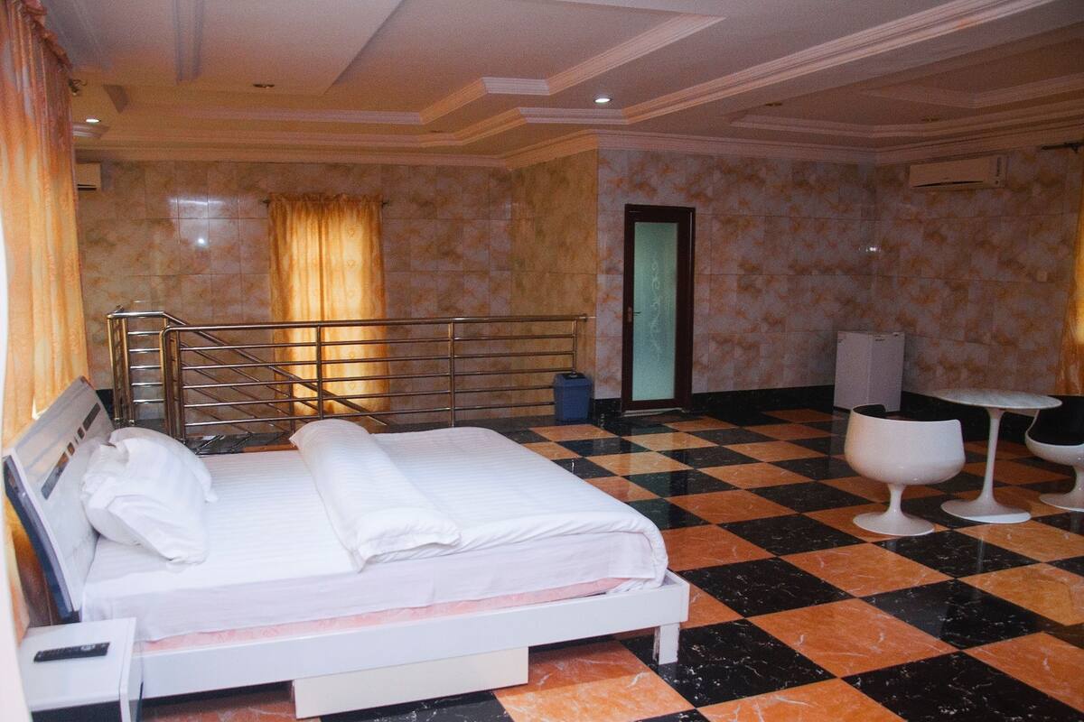Habitación de hotel con piso a cuadros, una cama con ropa blanca, una mesita con dos sillas y un equipo de aire acondicionado en la pared.