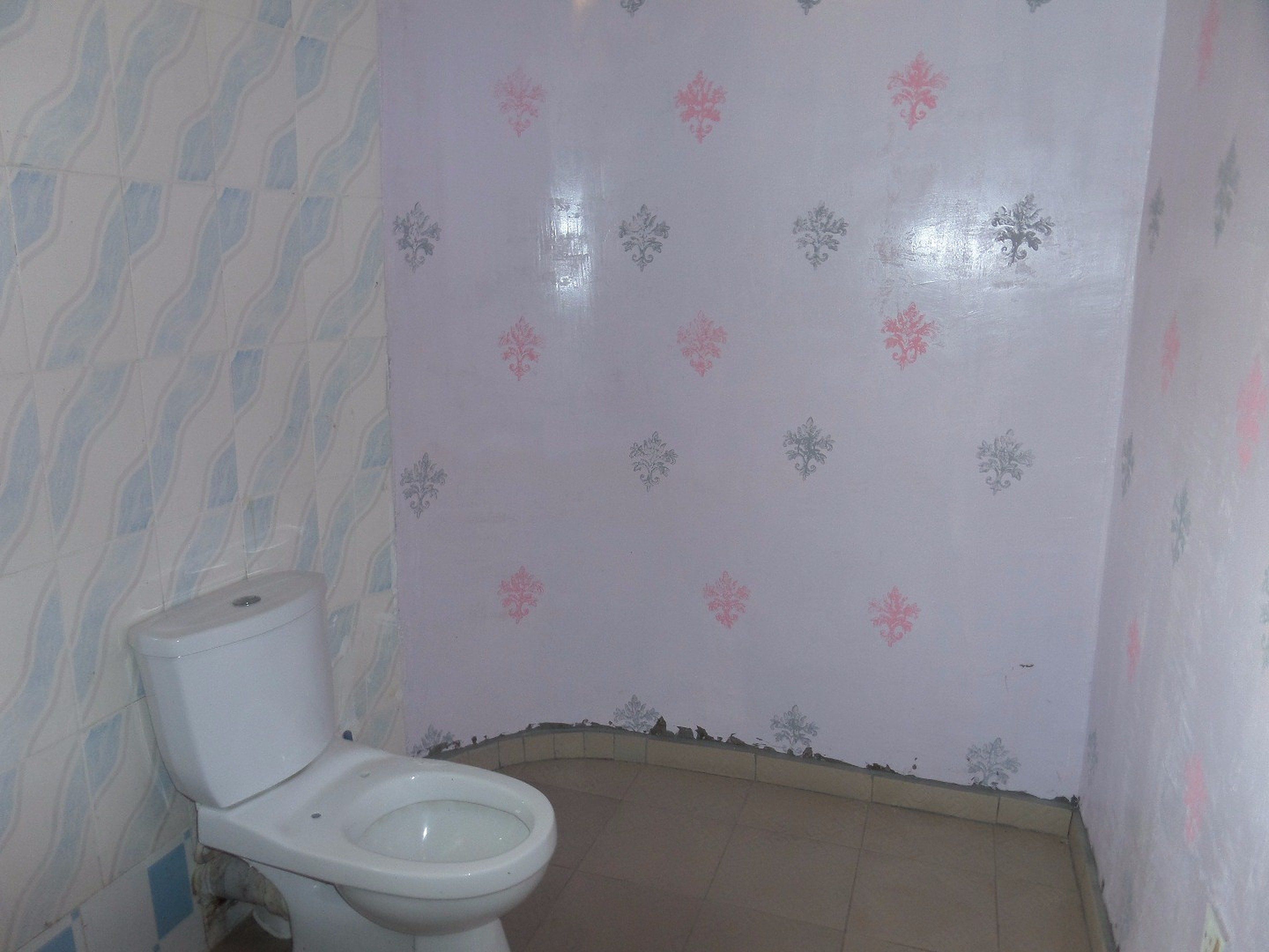 A bathroom with a toilet, patterned walls, and a tiled floor.