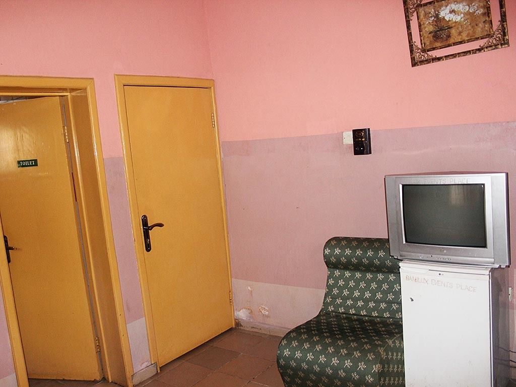 A room with two yellow doors marked "TOILET," a television on a stand, and a wall-mounted electrical outlet.