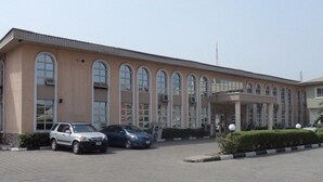 A building with a row of arched windows and a covered entrance. There are cars parked in front. - Banilux Guest House (Lagos)