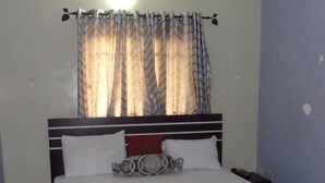 A bed with white bedding, a headboard with a red panel, and a window with patterned curtains. - Banilux Guest House (Lagos)