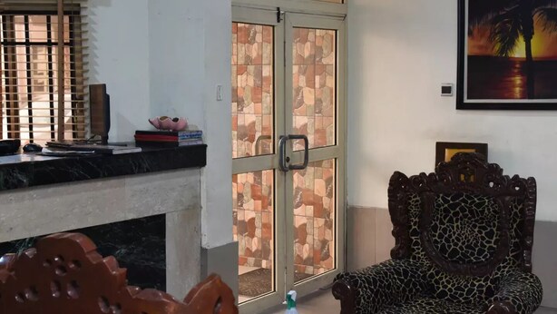 A living room with a fireplace, a dining table with chairs, a large window with a view, and a painting on the wall. - Banilux Guest House (Lagos)