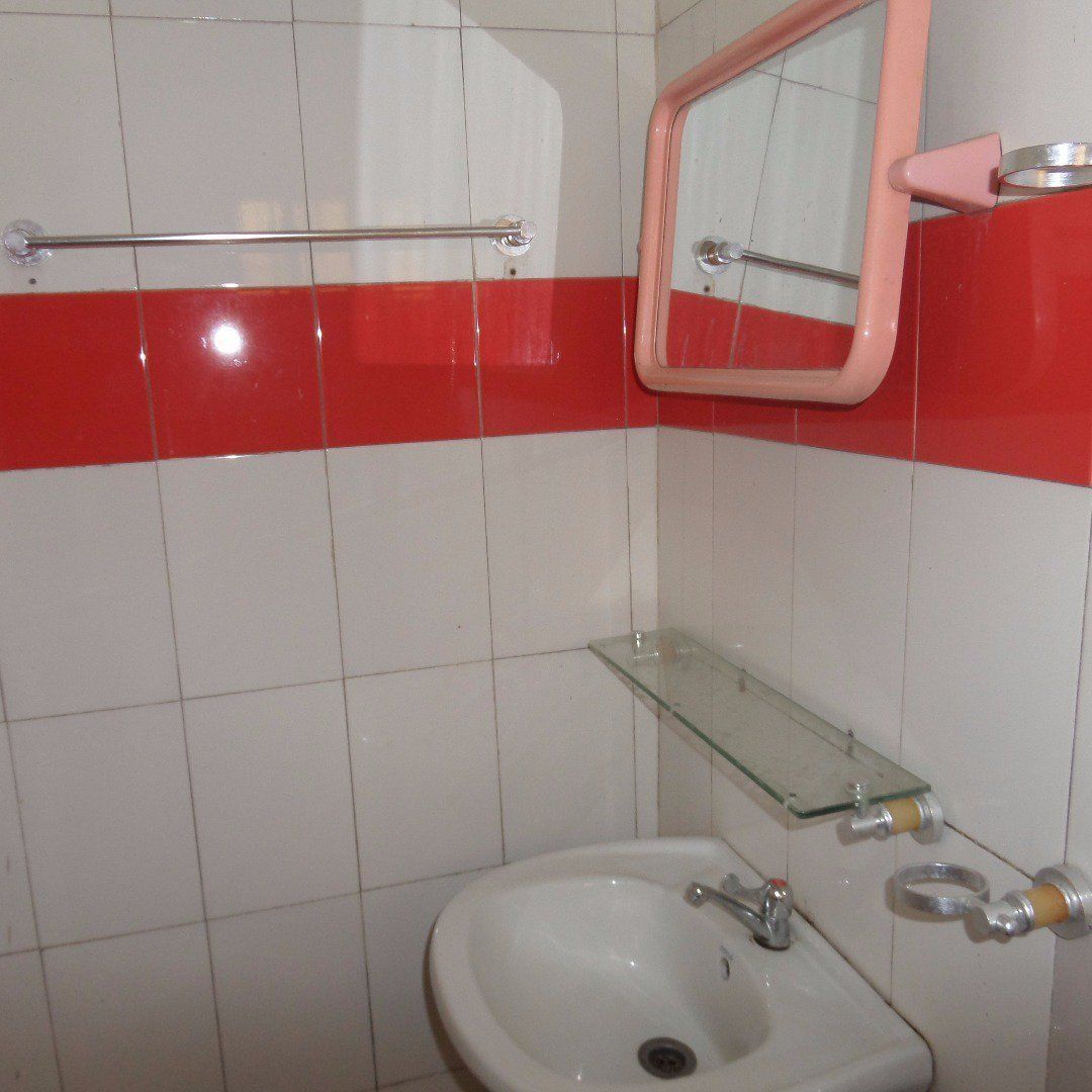 A bathroom with a white sink, a glass shelf, a towel rack, and a mirror with a pink frame.