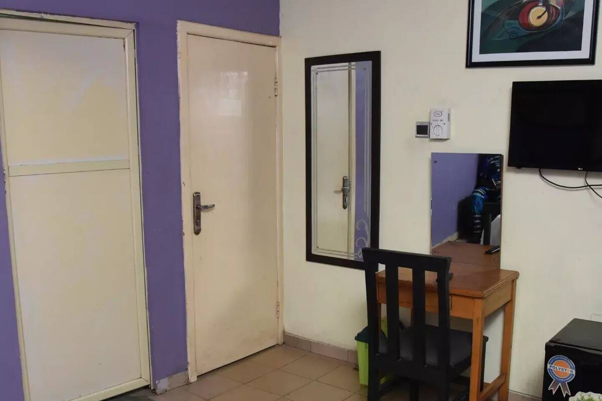 Una habitació amb llit, escriptori i cadira, televisió i una porta.