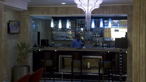 Zona de bar amb un barman, estantes plenes de garrafes, llums penjants i una gran lluminària decorativa.