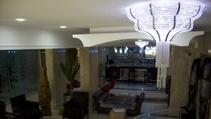 Un hall amb un llum modern, zona de seients amb sofàs i cadires, una recepció i una barra al fons.
