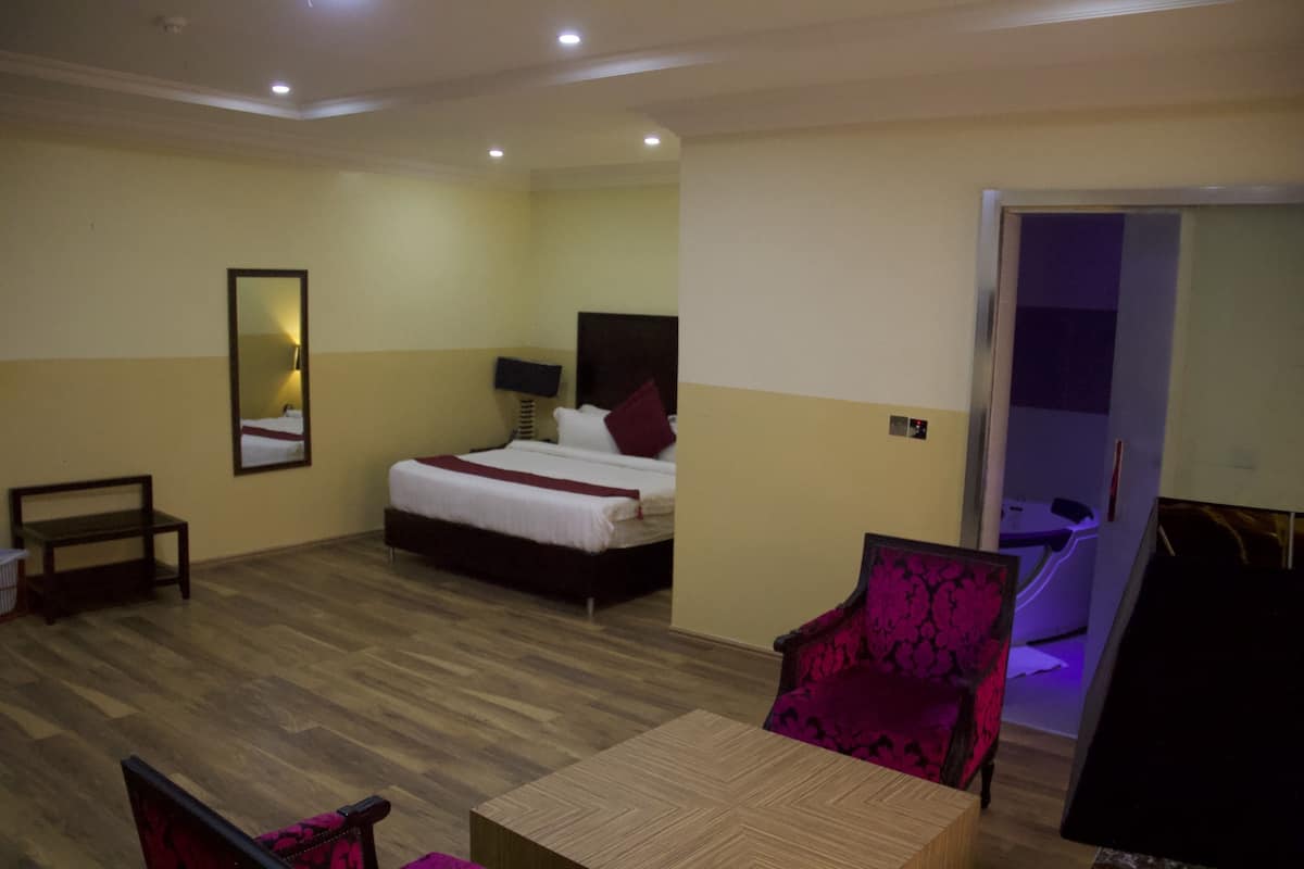A hotel room with a bed, a chair, a table, and a mirror.
