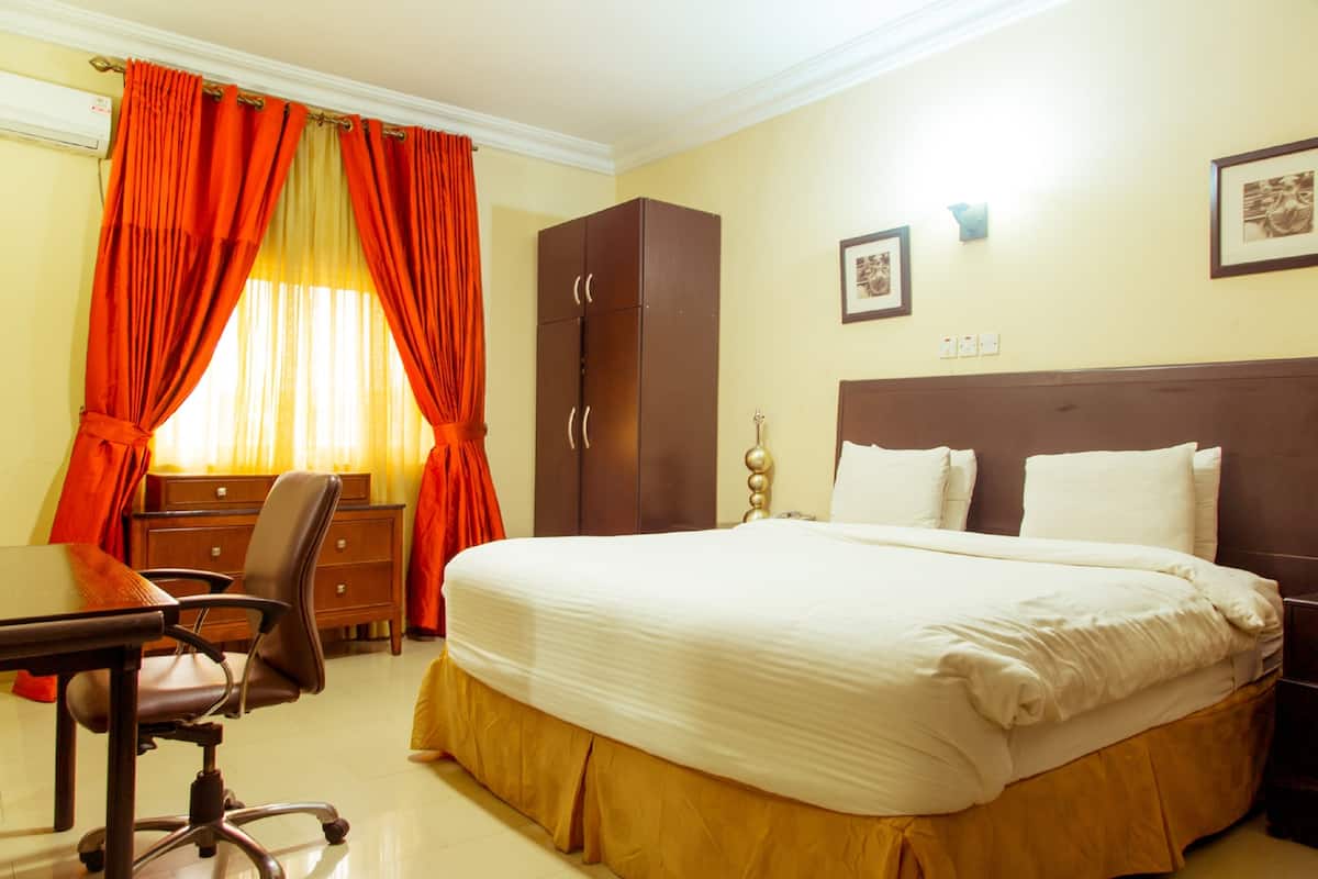 A hotel room with a large bed, a desk with a chair, a wardrobe, and a window with curtains.