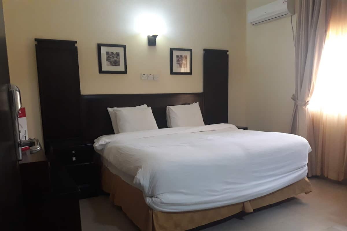 A hotel room with a large bed, a nightstand, a wall-mounted air conditioner, and two framed pictures above the bed.