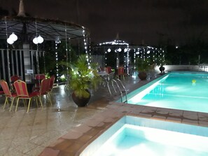 A pool area with chairs and tables, surrounded by string lights. - Hotel Reno (Abuja)