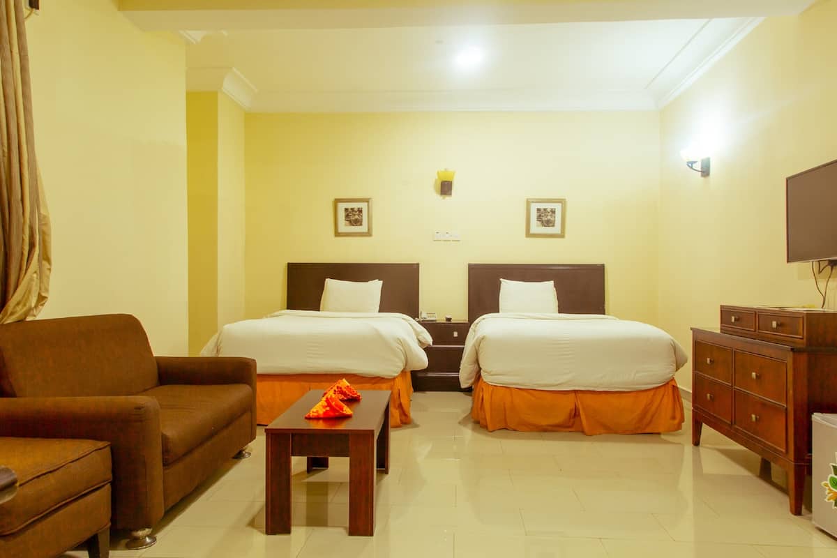 A hotel room with two beds, a sofa, a wooden table, and a TV.