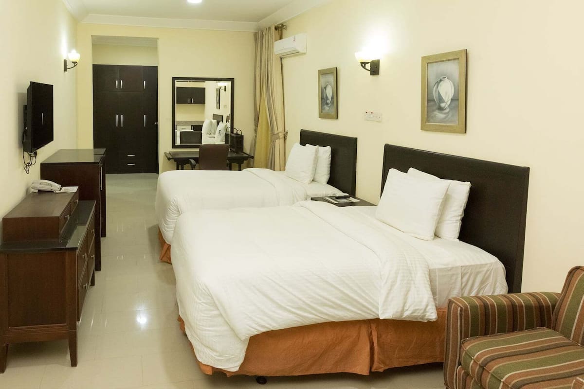 A hotel room with two beds, a desk, a chair, a television, and artwork on the walls.