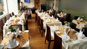 Un restaurant doté de nombreuses tables dressées pour le service, avec des nappes blanches, des couverts soigneusement disposés et des arrangements floraux en guise de décoration centrale.