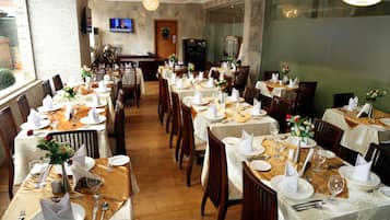 A restaurant with multiple tables set for dining, featuring white tablecloths, neatly arranged cutlery, and floral centerpieces.