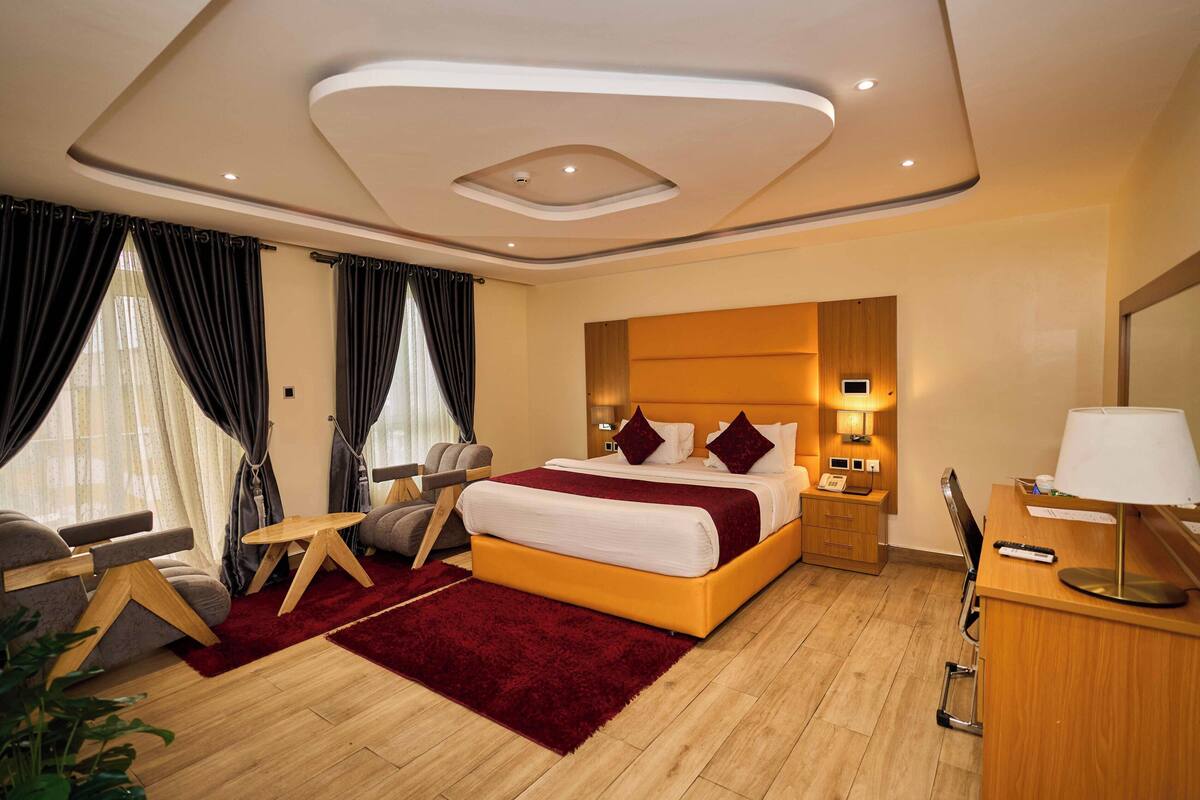 Quarto de hotel moderno com uma cama grande, uma escrivaninha, uma cadeira e uma mesinha.