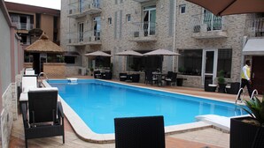 Une piscine entourée d’un bâtiment en pierre doté de balcons, avec des chaises longues et des parasols à proximité.