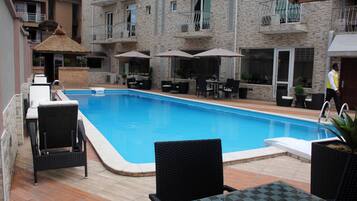 A swimming pool with lounge chairs and umbrellas, surrounded by a stone building with balconies.