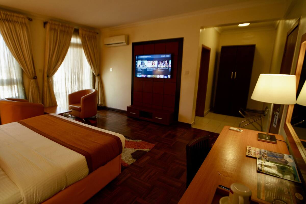 Quarto de hotel com uma cama grande, televisão, escrivaninha com luminária e uma cadeira.