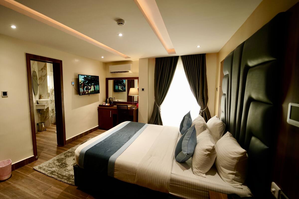 Quarto de hotel moderno com uma cama grande, uma escrivaninha, um espelho e uma televisão.