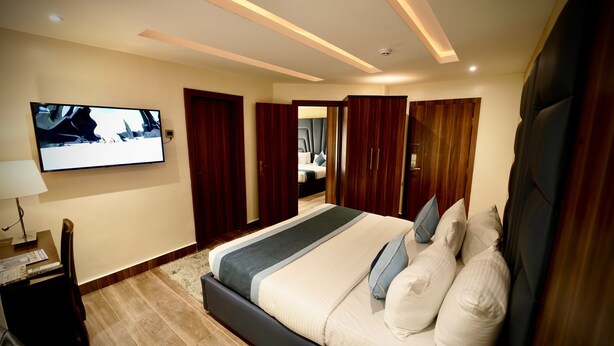 Une chambre d’hôtel moderne dotée d’un grand lit, d’un téléviseur à écran plat fixé au mur et d’une armoire en bois.