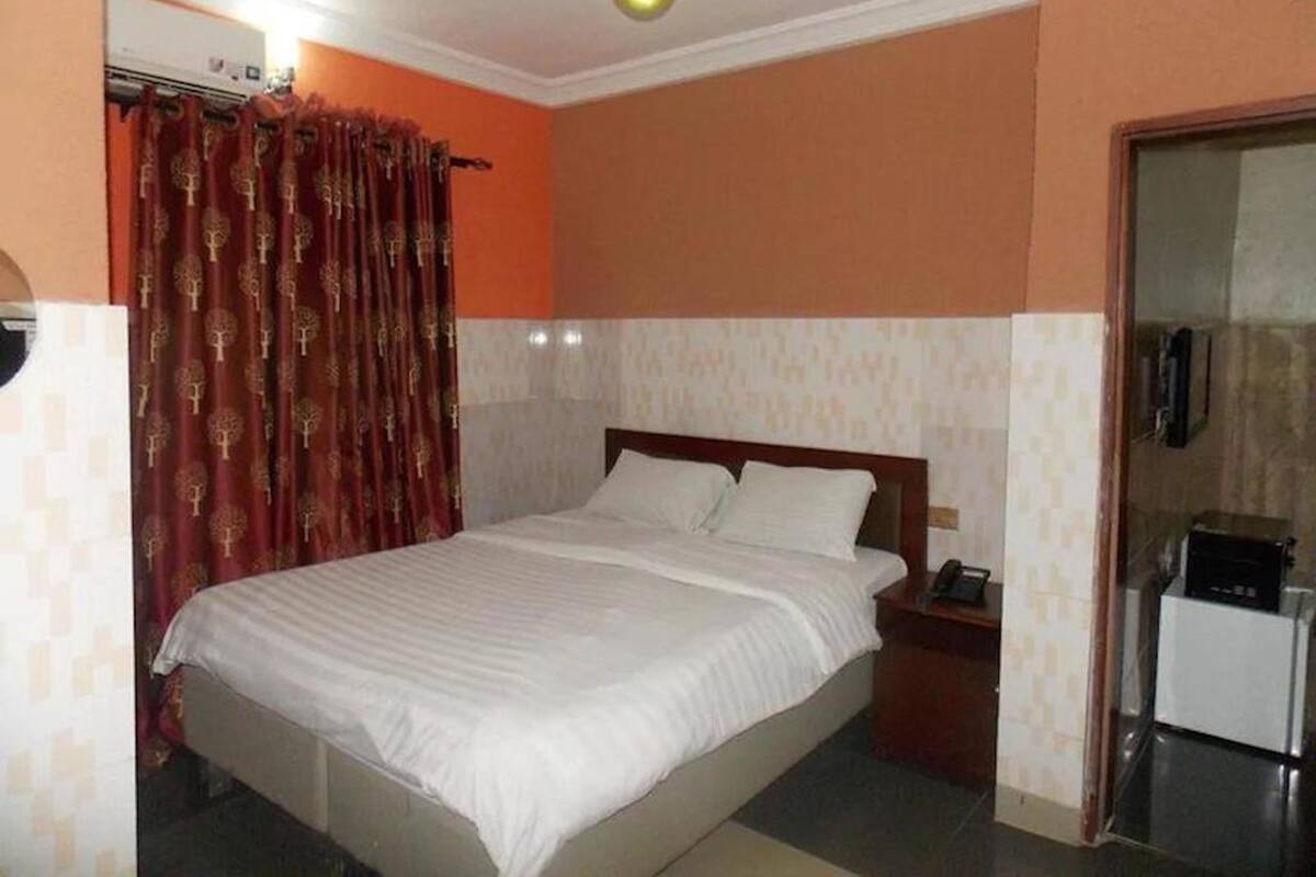 Quarto com cama, mesa de cabeceira, telefone e porta que dá para uma kitchenette.