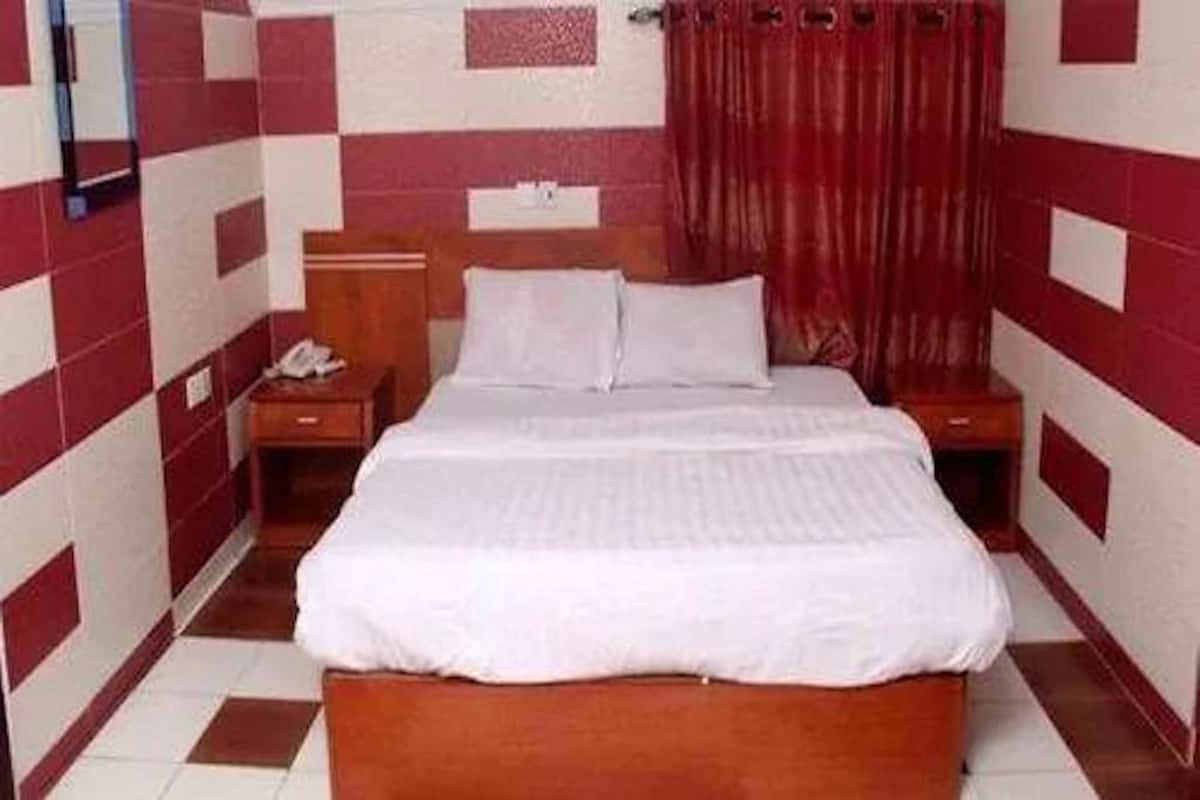 Quarto pequeno e bem arrumado, com uma cama de casal, mesa de cabeceira e cabeceira de madeira.