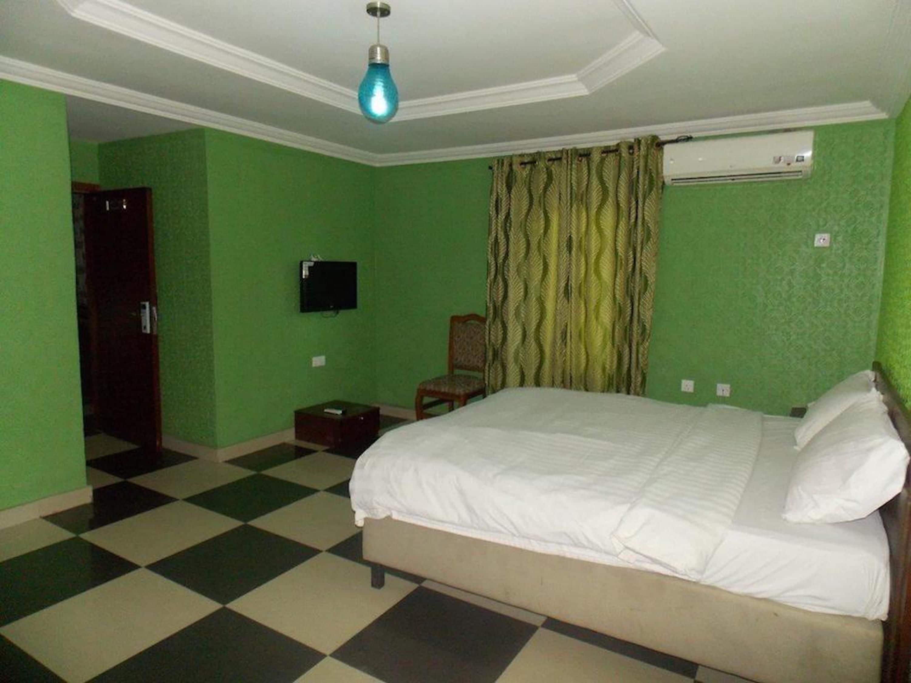 A bedroom with a bed, a television, a chair, and an air conditioning unit.