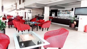 A spacious lobby with red upholstered seating, a bar area with a television, and a staircase in the background. - Pelican Hotel Lekki (Lekki)