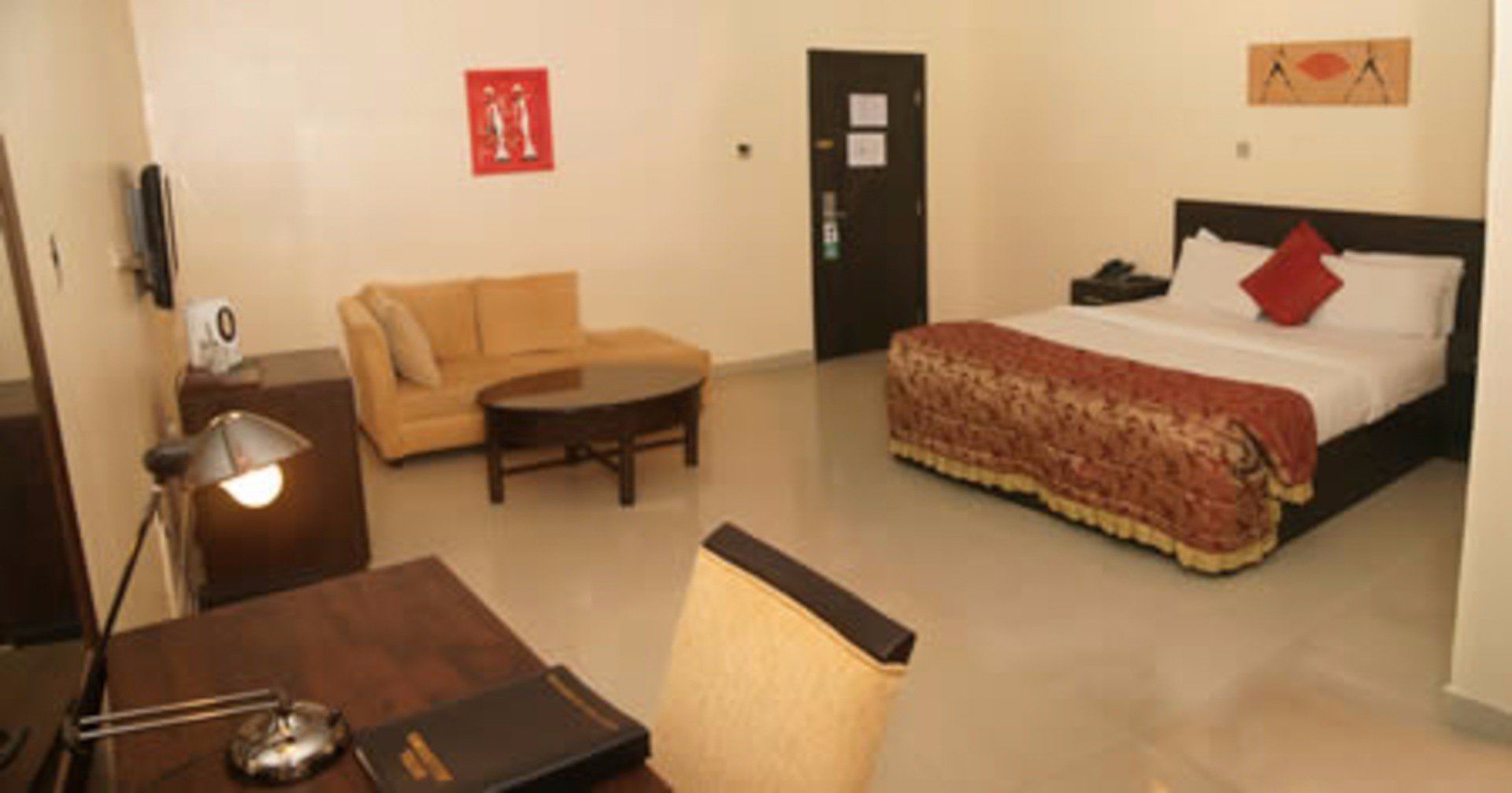 A hotel room with a bed, a sofa, a desk with a lamp, and a chair.