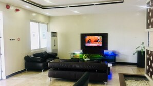 A modern living room with a flat-screen TV, leather sofas, a coffee table, and a decorative plant. - Pelican Hotel Lekki (Lekki)