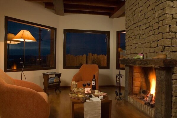 A cozy room with a stone fireplace, a table with food and drinks, and large windows with night views.