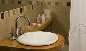A bathroom with a round sink, a mirror, and a shelf with toiletries. - Hosteria Roble Sur (El Calafate)