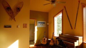 Una habitación con ventilador de techo, un piano, guitarras y una tabla de surf en la pared.