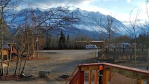 Una terraza de madera con sillas, una planta en maceta y vistas de montañas nevadas.