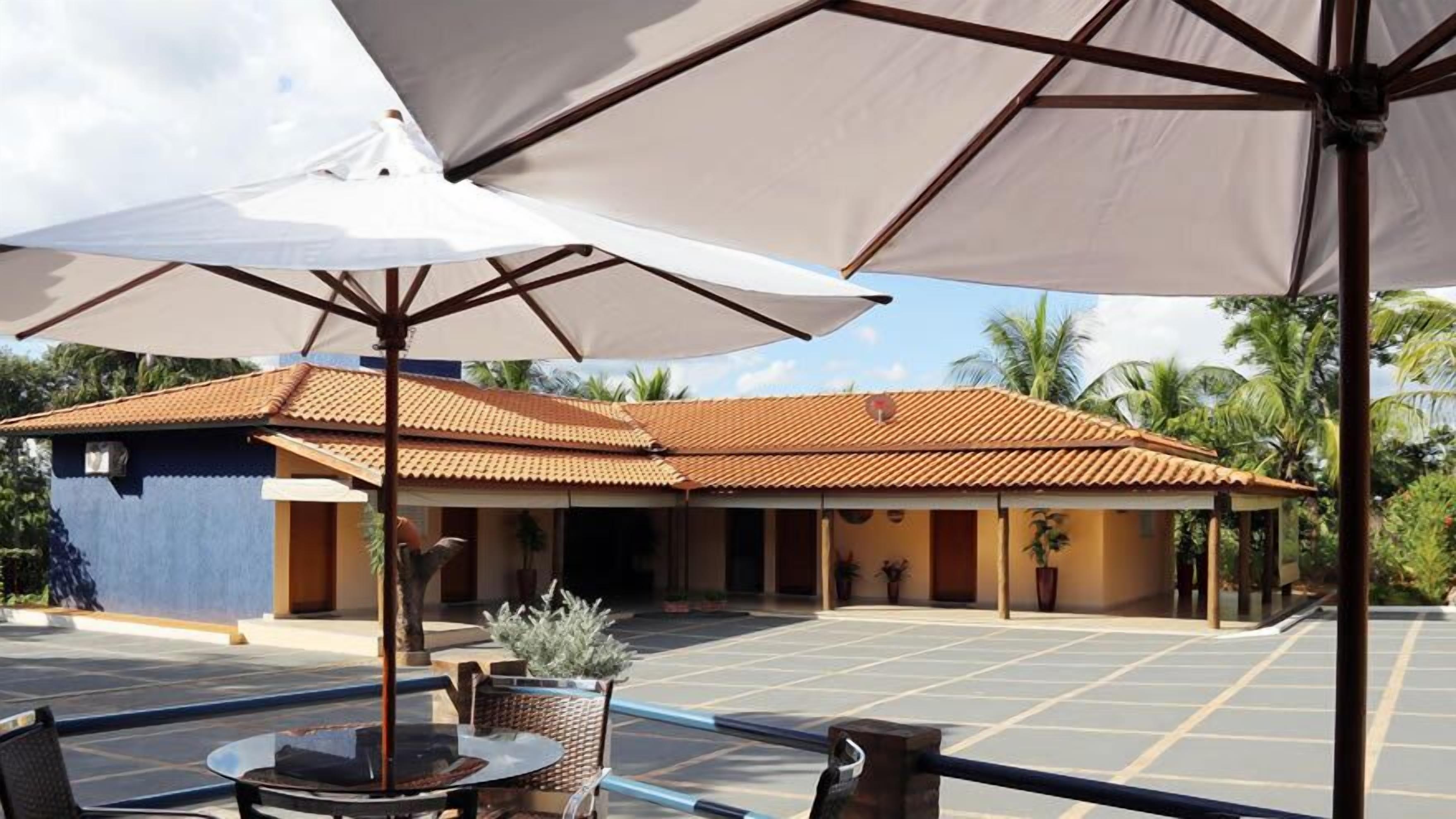 A hotel with a tiled roof, outdoor seating area with umbrellas, and a parking lot.