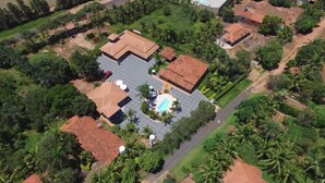 An aerial view of a residential area with multiple houses, a swimming pool, and lush greenery. - Pousada Recanto Solar dos Passaros (Olímpia)