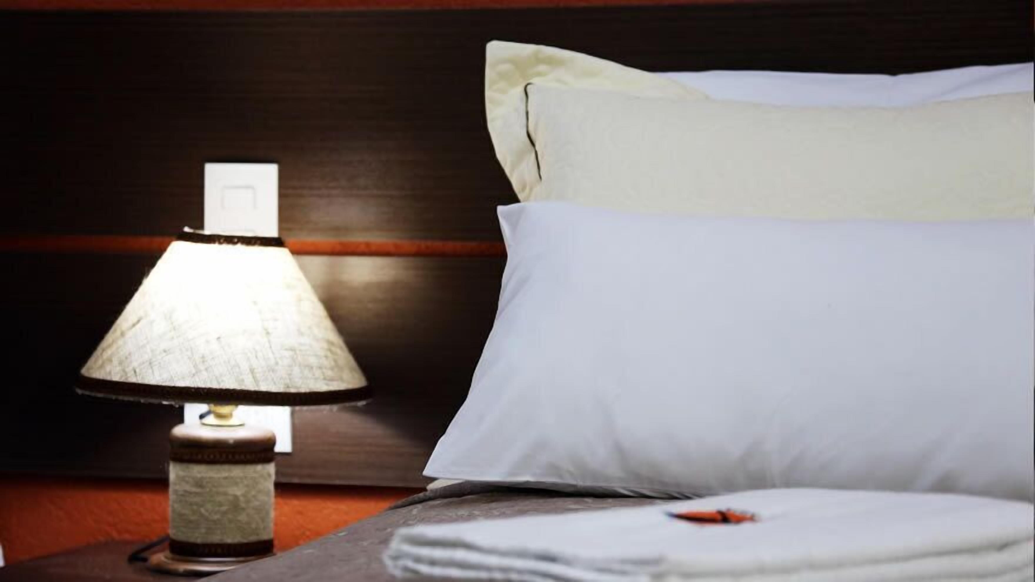 A neatly made bed with white pillows and a lamp on a wooden nightstand.